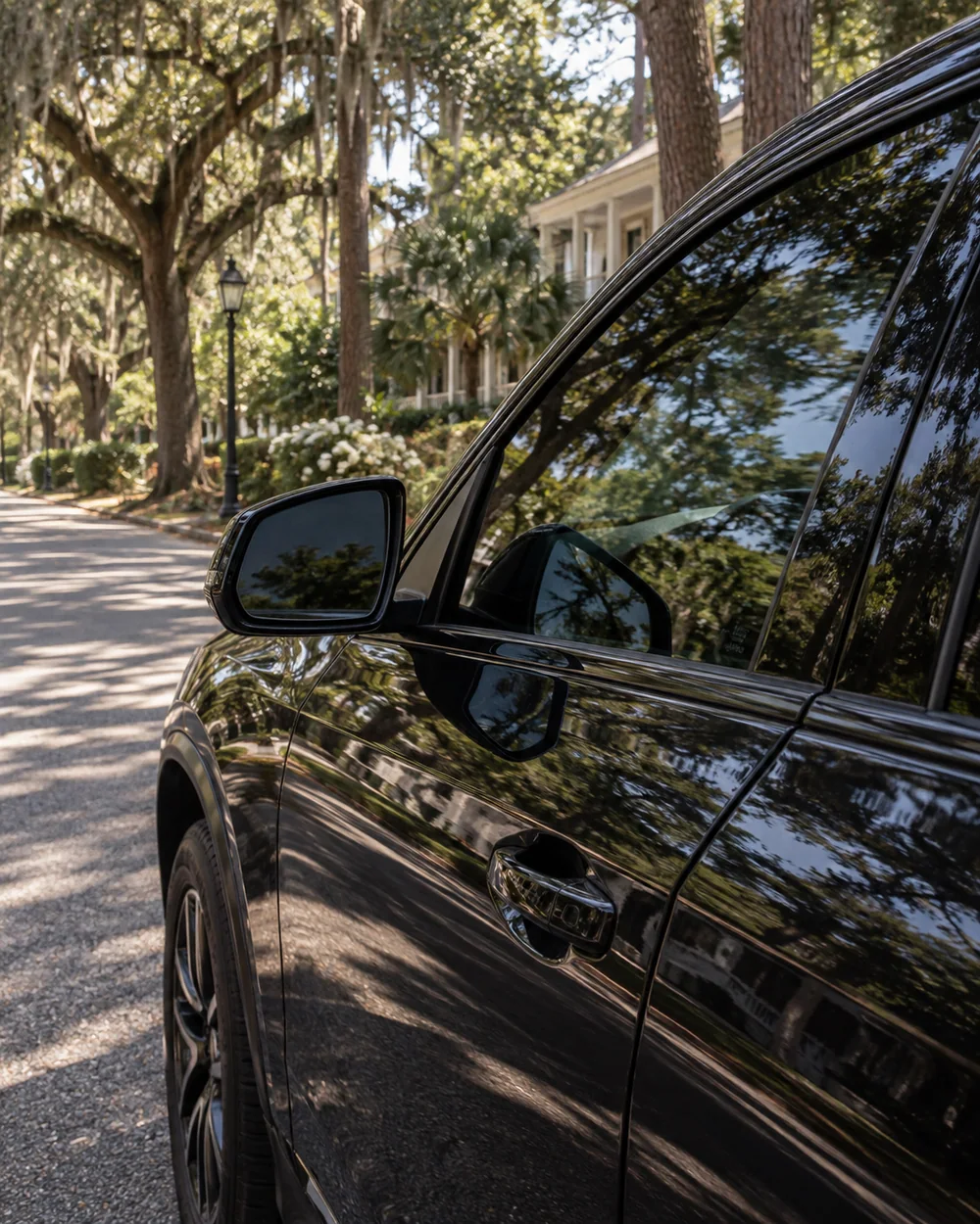 Tinted black vehicle reflecting mature pines and live-oak shade in Summerville